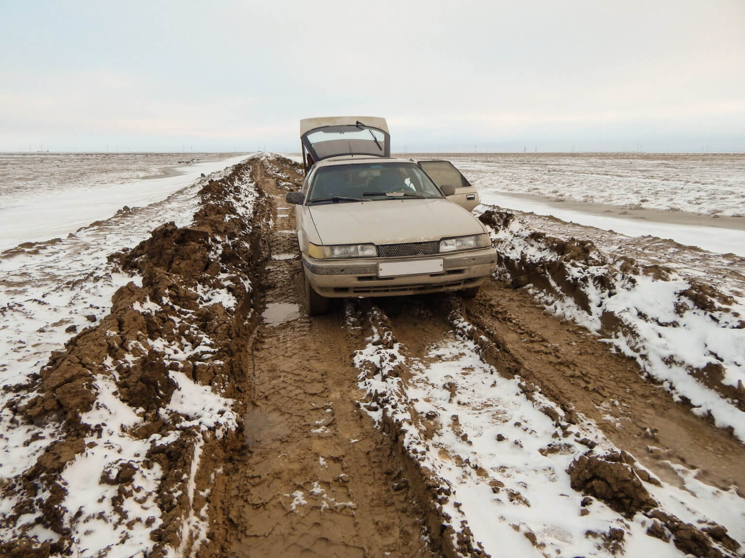 A car broken down on a very muddy rural road outside of Atyrau, in winter.