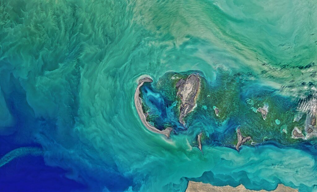 Tyuleniy Archipelago seen from space with colourful water and marshes.